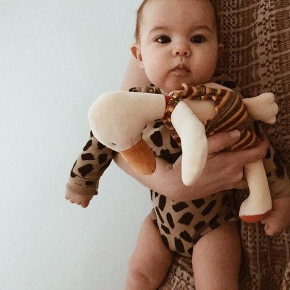 baby holding soft toy duck with mothers arm